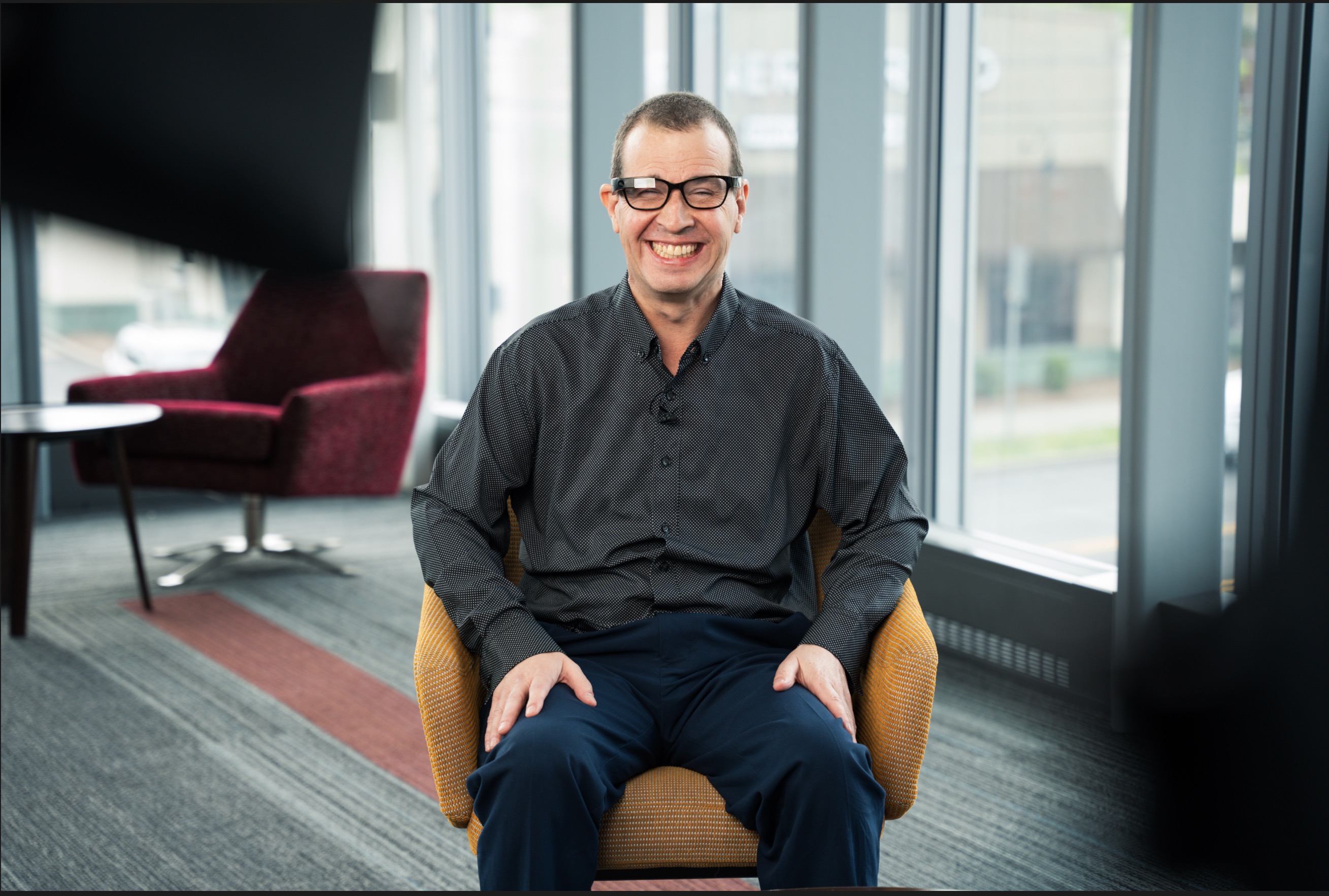 Shawn Keen sitting and smiling, wearing Envision smart glasses